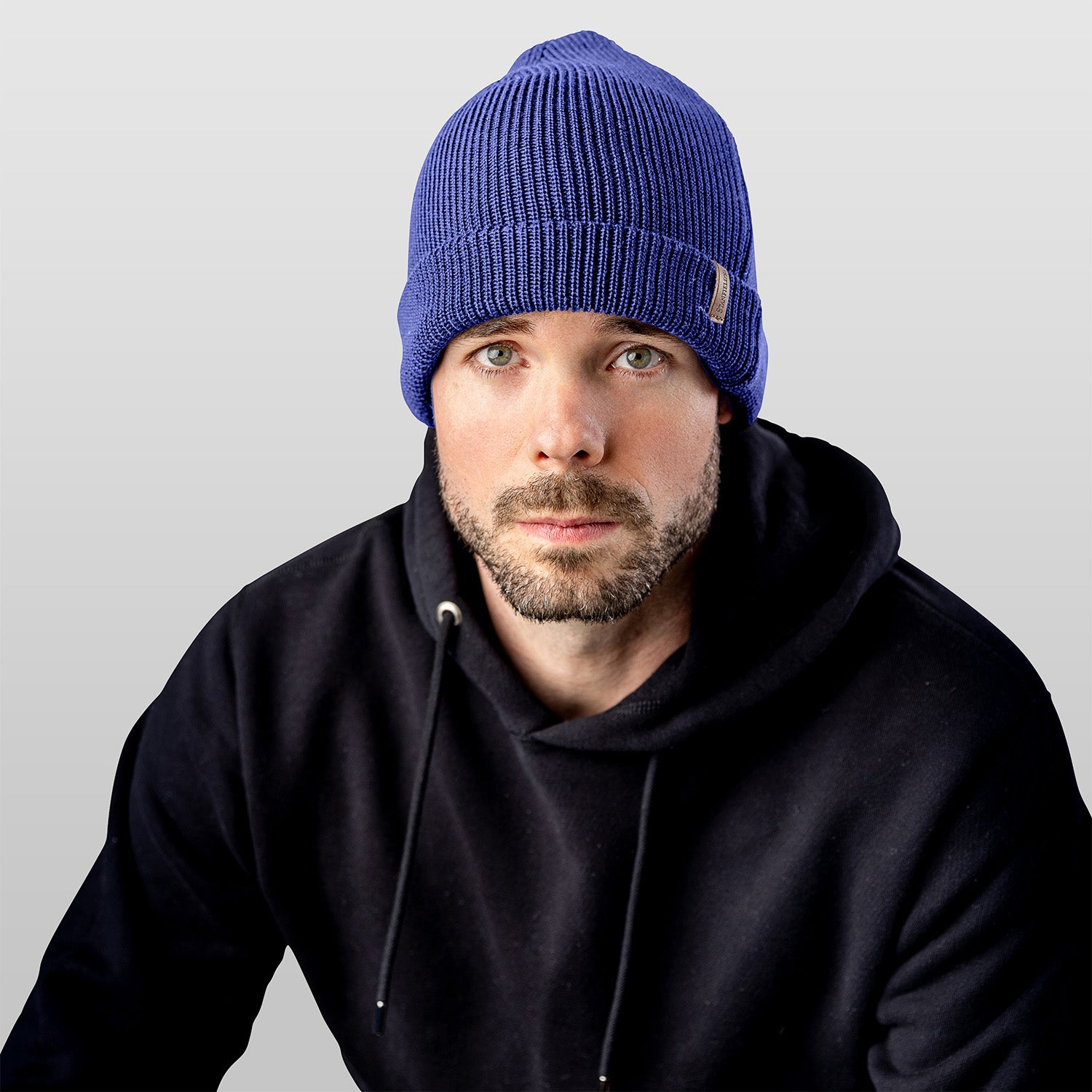 Man wearing a blue beanie and black hoodie against a gray background